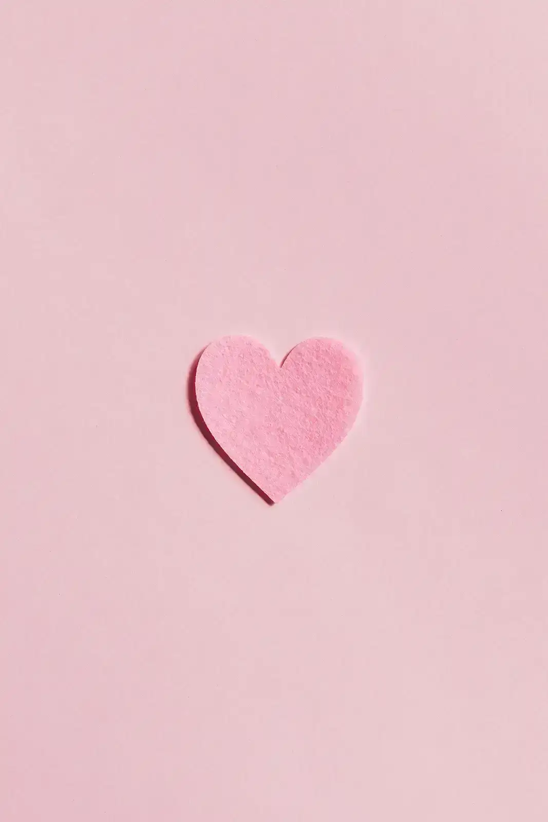 A pink felt-cloth heart on a pink background.